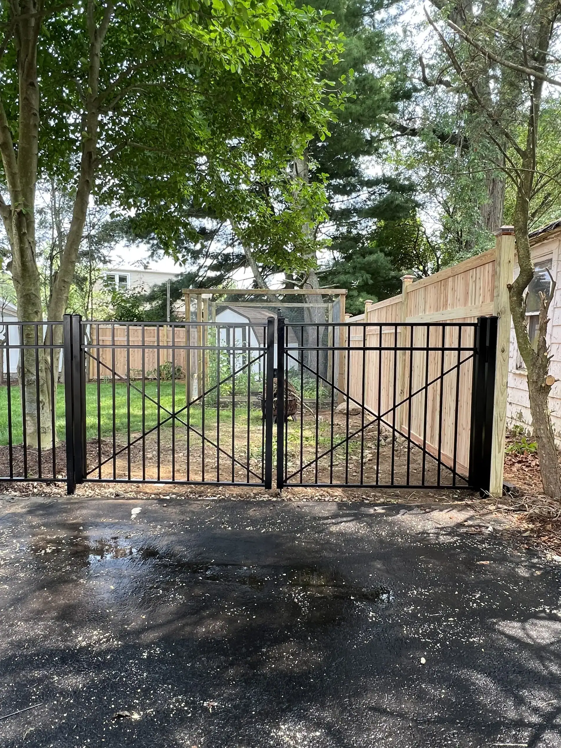 Double black aluminum driveway gate next to a wood privacy fence