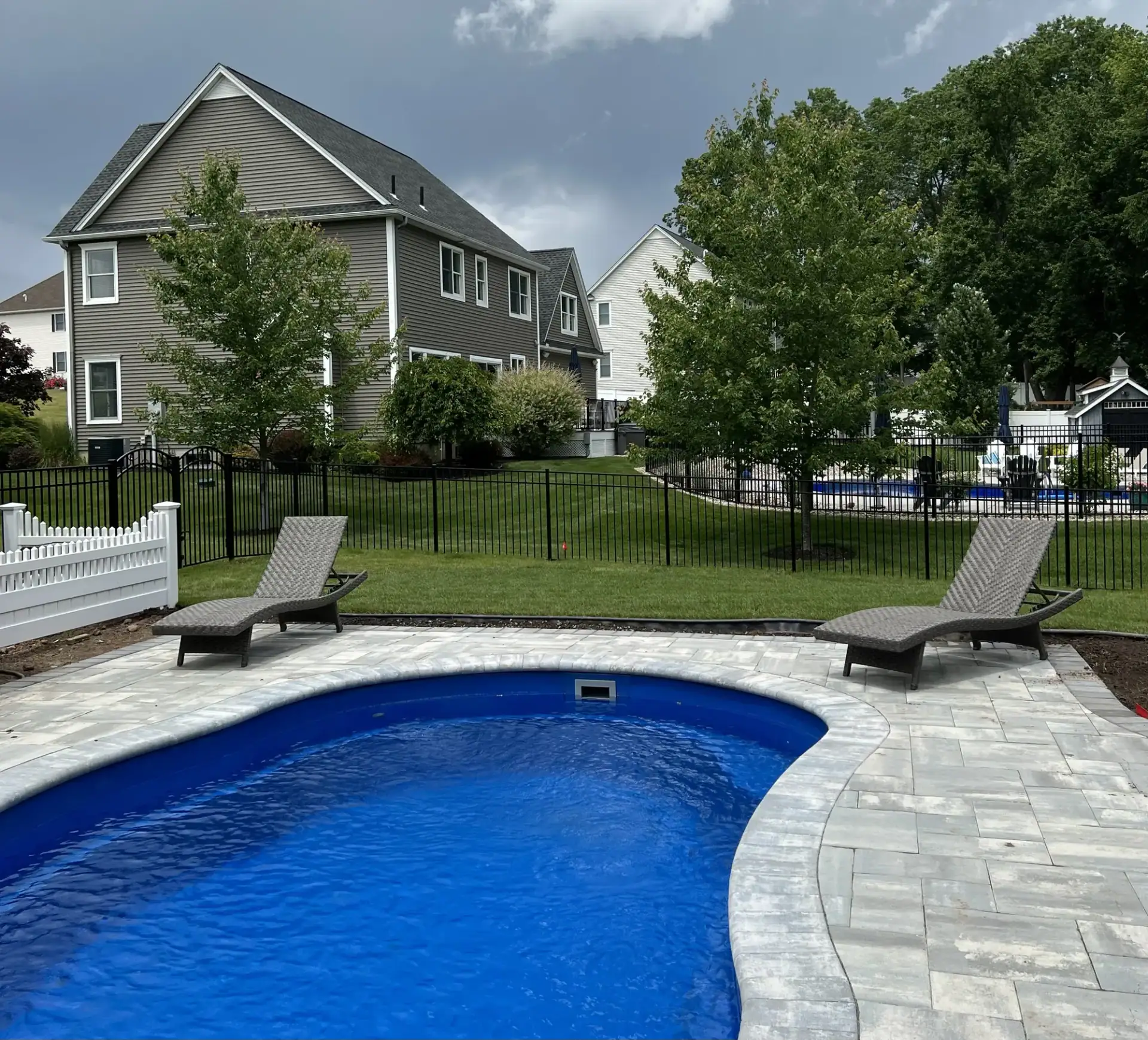Black aluminum pool fence around an in-ground pool with a paver deck
