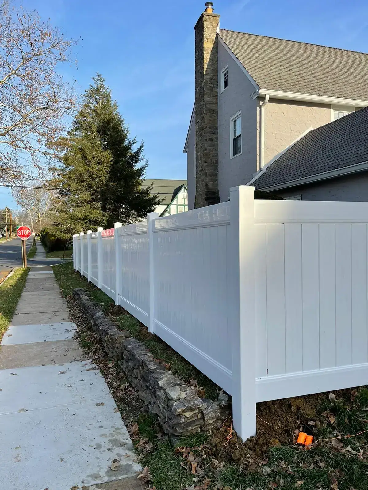 White vinyl privacy fence set above a stone wall along a sidewalk